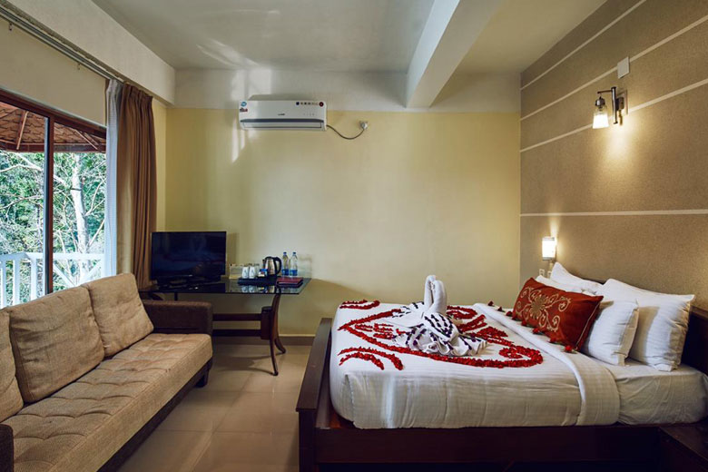 “Cozy honeymoon cottage bedroom at Southern Panorama Indriya in Munnar, featuring warm wooden interiors, soft lighting, and a private terrace overlooking the misty hills.”