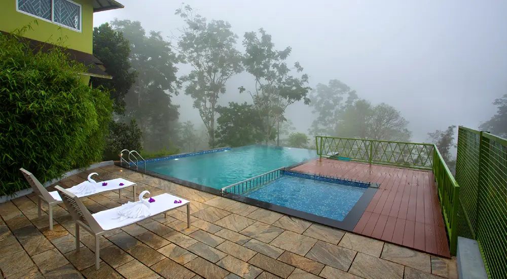Infinity swimming pool at Amrezy Resort in Vythiri, Wayanad with misty mountain and forest views