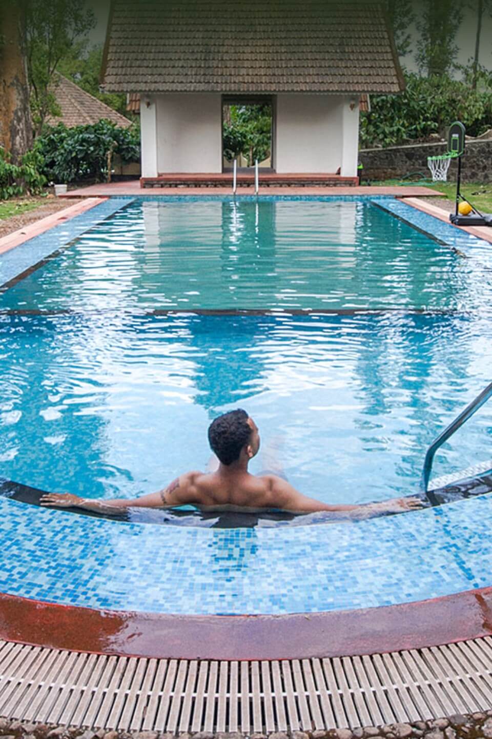 Open-air swimming pool at Misty Woods Resort in Coorg overlooking misty hills and lush green plantations under clear mountain skies.