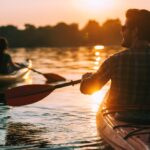 Meeting sunset on kayaks. Rear view of young couple kayaking on lake together with sunset in the backgrounds
