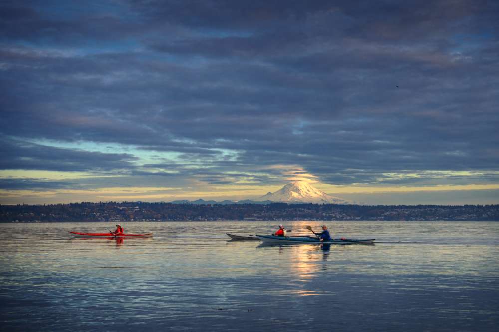 Boats sailing on calm backwaters surrounded by lush greenery and distant hills during a golden sunset.