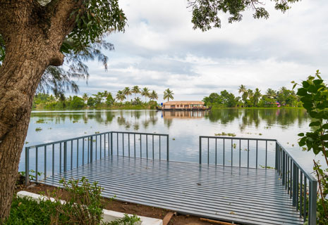 Panoramic lake view of Vembanad Lake from Warmth Lake Haven Island Resort in Alleppey, showcasing serene backwaters, swaying coconut palms, and golden sunset reflections.