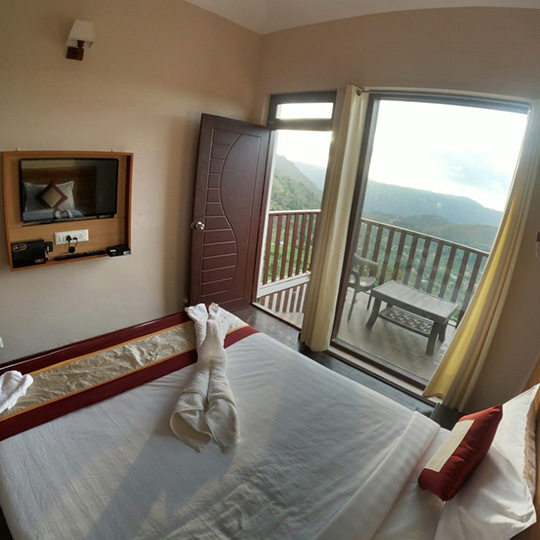 Comfortable balcony room at Warmth Hill Crest, Kodaikanal, featuring cozy interiors and a mesmerizing valley view overlooking misty hills and lush green landscapes.